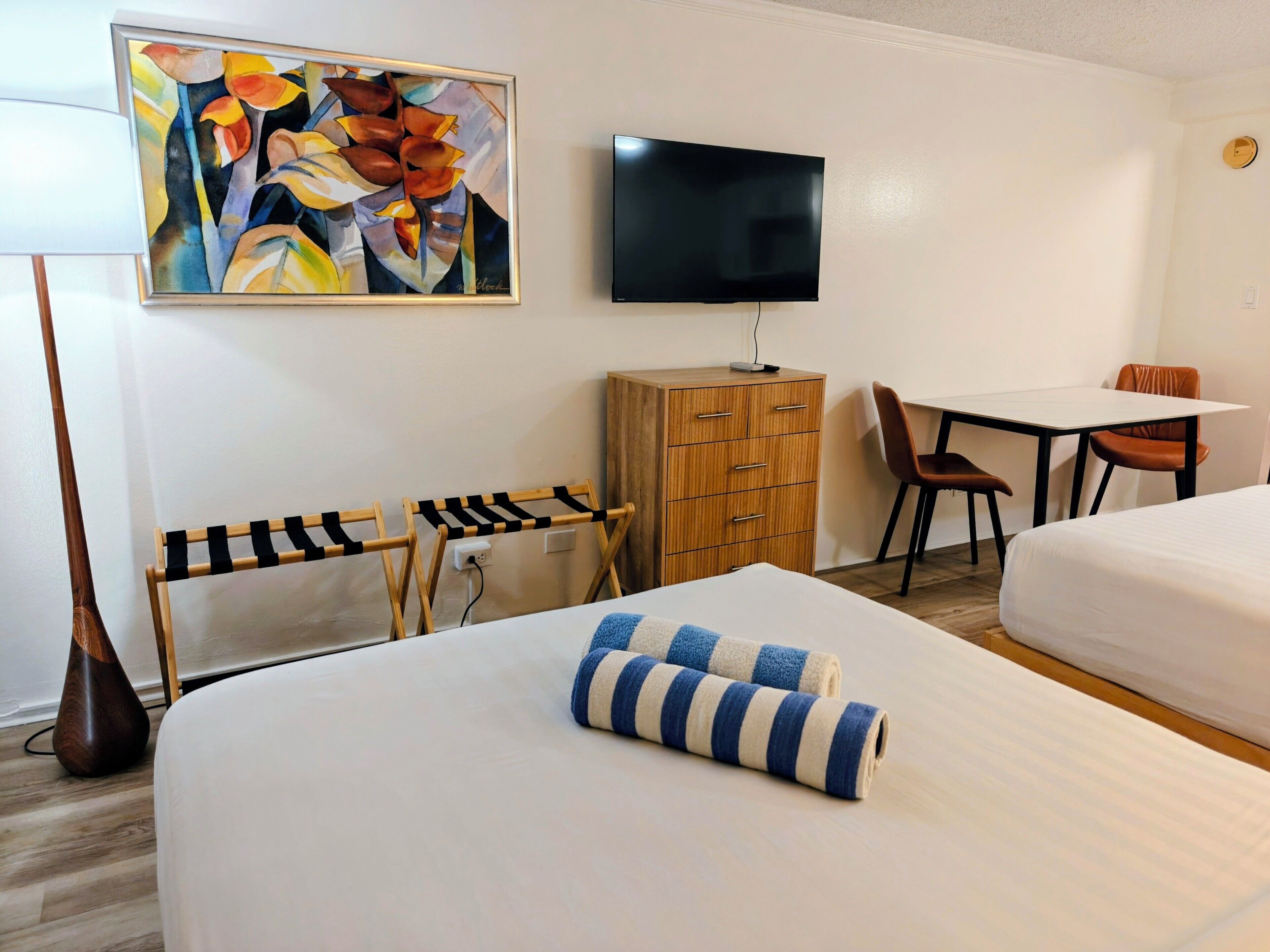 A hotel room with two beds, a wooden dresser, a desk with a chair, a flat-screen TV, and a painting on the wall.