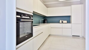 A modern kitchen with white cabinets, a black oven, a coffee maker, and a toaster. - T3 Large Terrace "Capo di Feno" (Ajaccio)