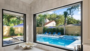 Un baño moderno con un ventanal grande que da a una piscina y una terraza de madera.