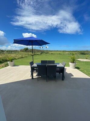 Une terrasse extérieure avec une table et des chaises, un parasol bleu et des plantes en pot.