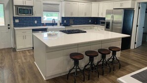 A modern kitchen with white cabinets, a large island with stools, a microwave, and a refrigerator.