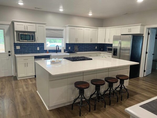 A modern kitchen with white cabinets, a large island with stools, a microwave, and a refrigerator. - Enjoy "The Lake Life" at Kentucky Lake! (Buchanan)
