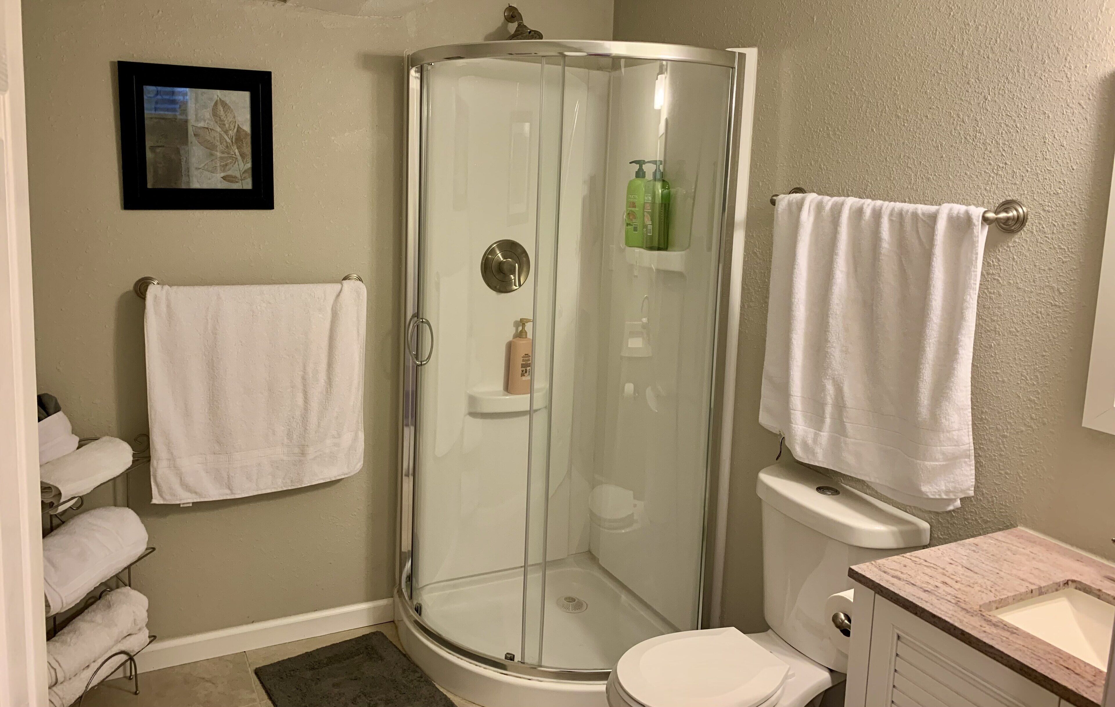 A bathroom with a glass-enclosed shower, a toilet, a sink, and two white towels hanging on the wall.