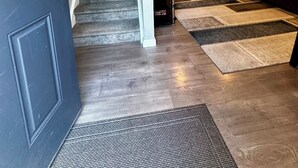 Una escalera conduce a una sala de estar con una puerta oscura, un sofá de color oscuro y una alfombra estampada.