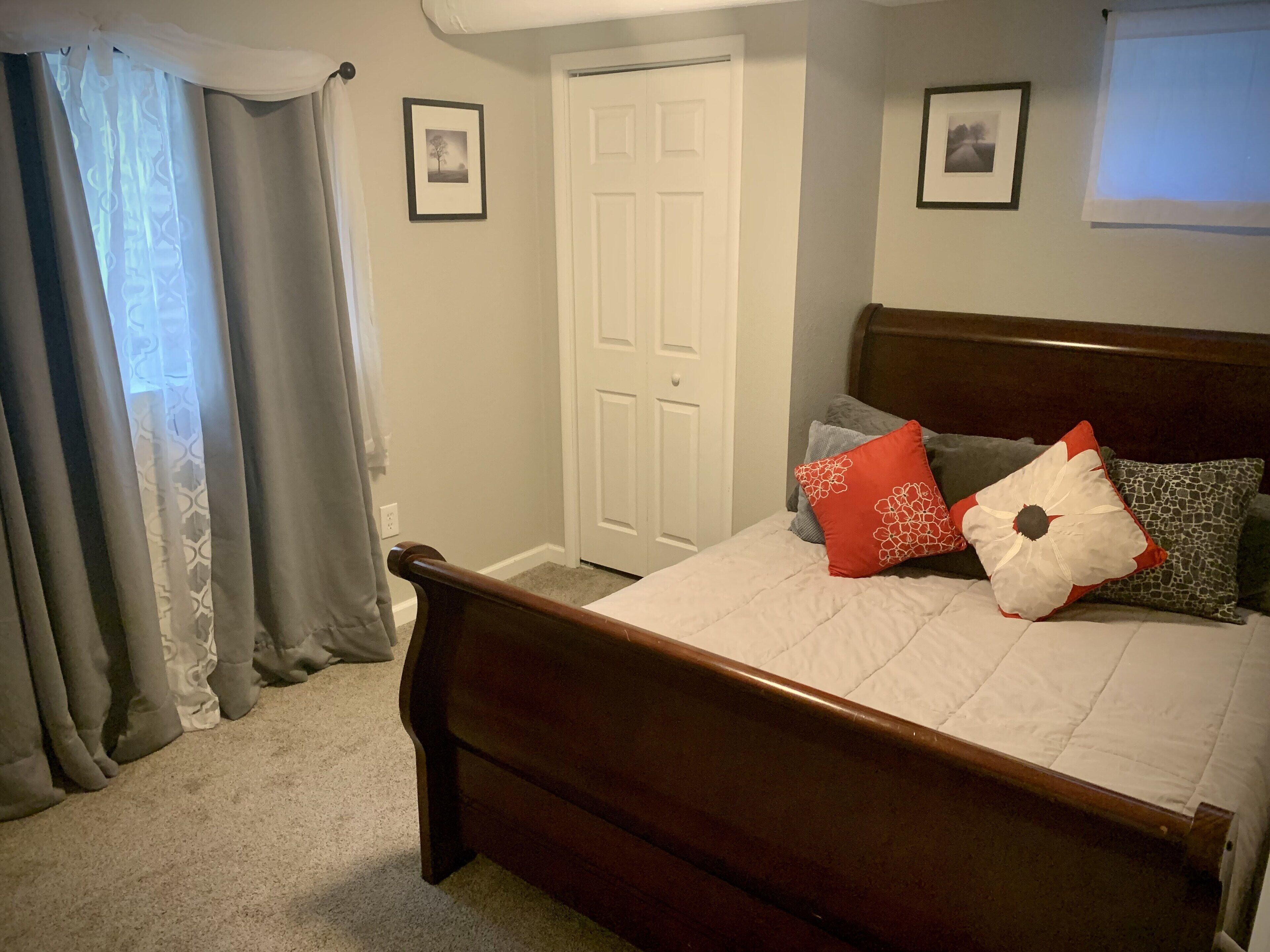 Une chambre avec un lit en bois, une porte blanche et deux tableaux encadrés accrochés au mur.