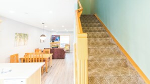 Una escalera con alfombra estampada y barandilla de madera, que conduce a una habitación con comedor y cocina al fondo.