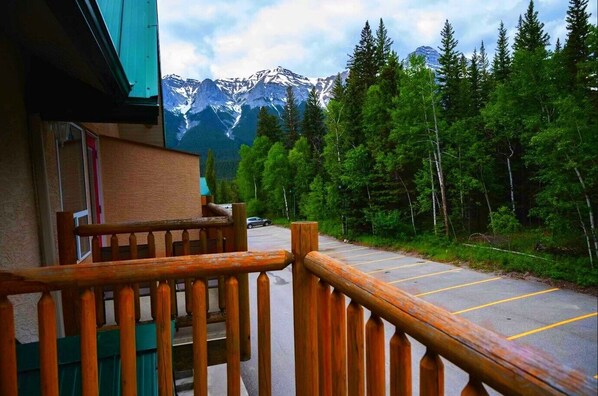 Un balcón de madera con vistas a un estacionamiento y una cordillera boscosa.