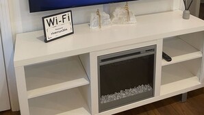 Un televisor de pantalla plana sobre un mueble blanco de entretenimiento con un cartel que indica la contraseña de Wi-Fi.