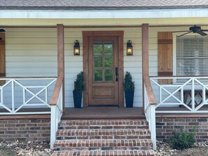 A house with a wooden front door, two potted plants, and a porch with white railings.