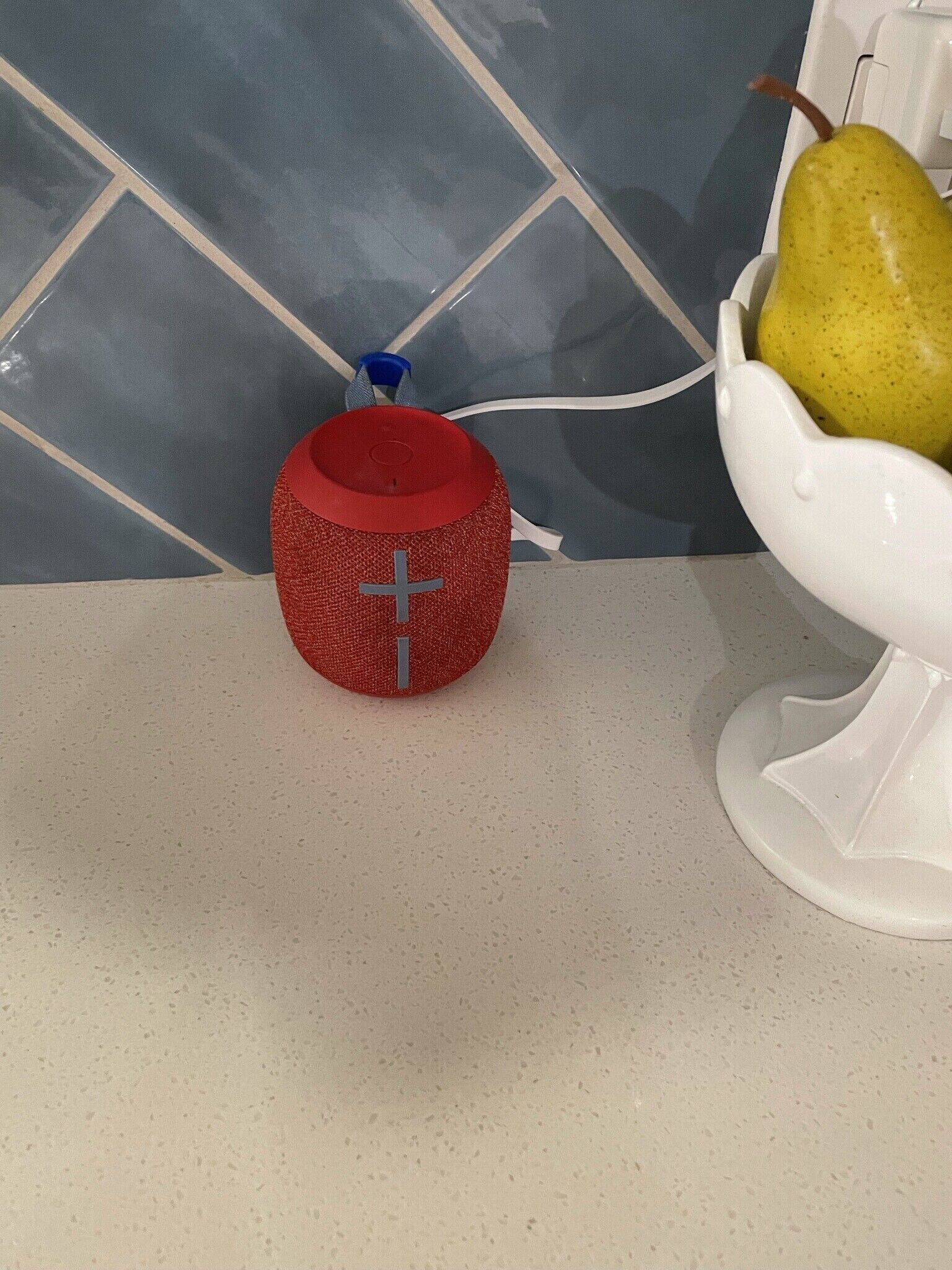 A red speaker with a cross symbol on a countertop next to a white bowl with a pear.
