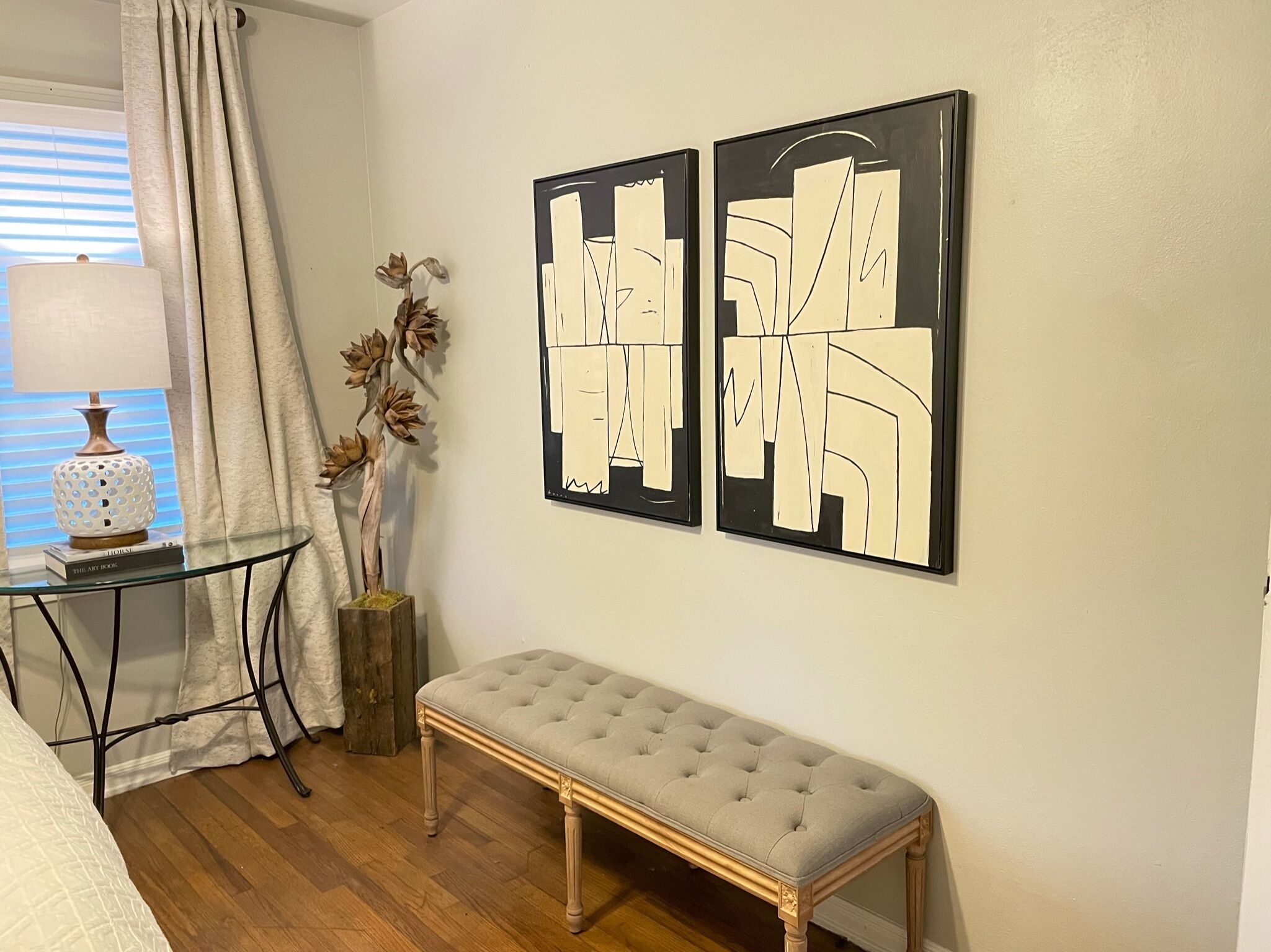 Une pièce avec une table en verre, un banc et deux tableaux abstraits accrochés au mur.