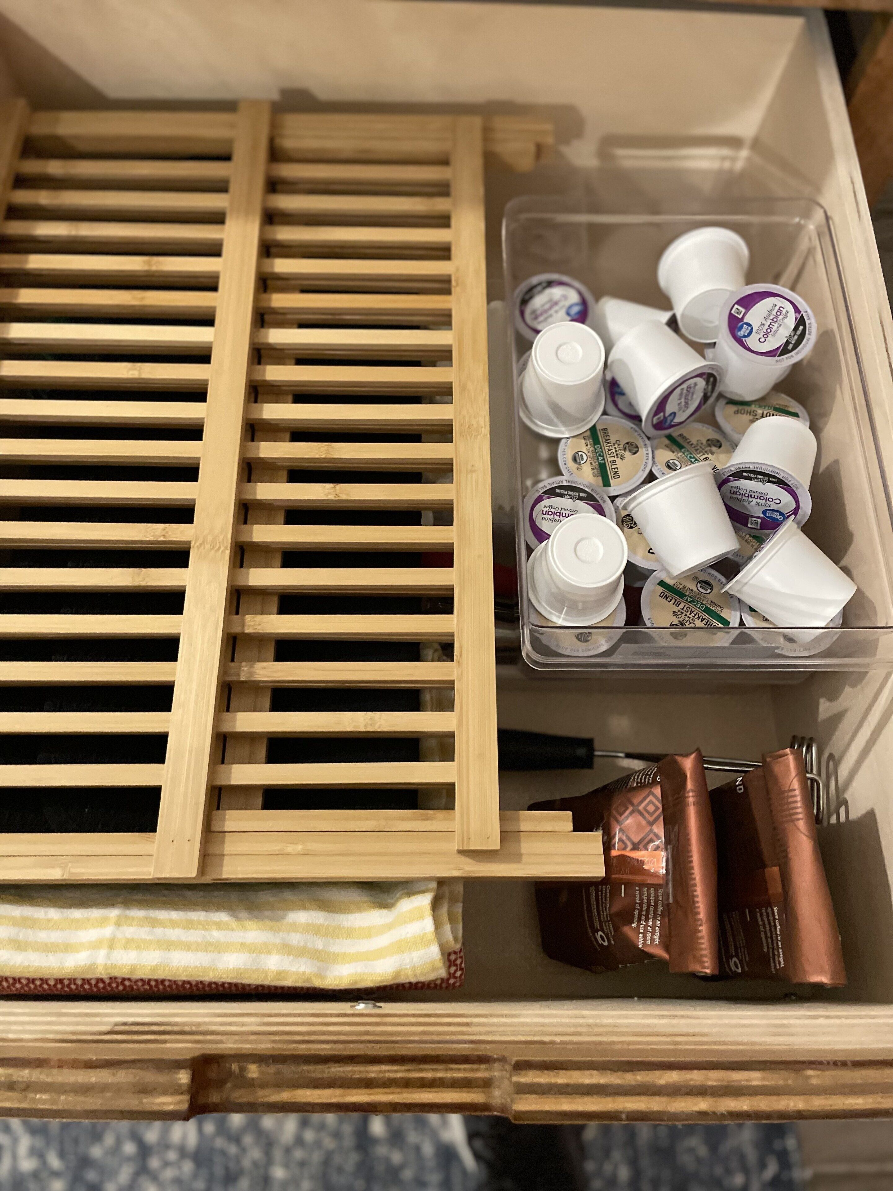 Un cajón de madera con un recipiente de plástico que contiene varios objetos, entre ellos botellas con etiquetas blancas y moradas, y algunos paquetes marrones.