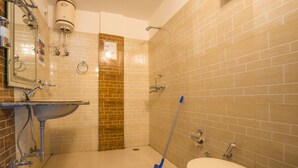 A bathroom with a sink, toilet, shower, and a mop leaning against the wall.