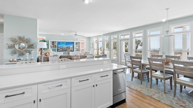 A spacious kitchen with a large island, white cabinetry, and a dining area with wooden chairs and a table.