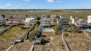 A coastal residential area with houses connected by wooden walkways, a swimming pool, and a view of the ocean.