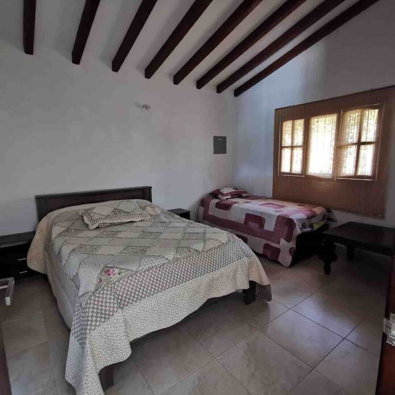 Une chambre avec un grand lit, un plus petit lit et une fenêtre avec des rideaux.