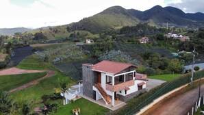 A modern two-story house with a stone facade, a red-tiled roof, and a balcony. It is surrounded by lush greenery and hills in the background. - Country house surrounded by nature  (El Carmen de Viboral)
