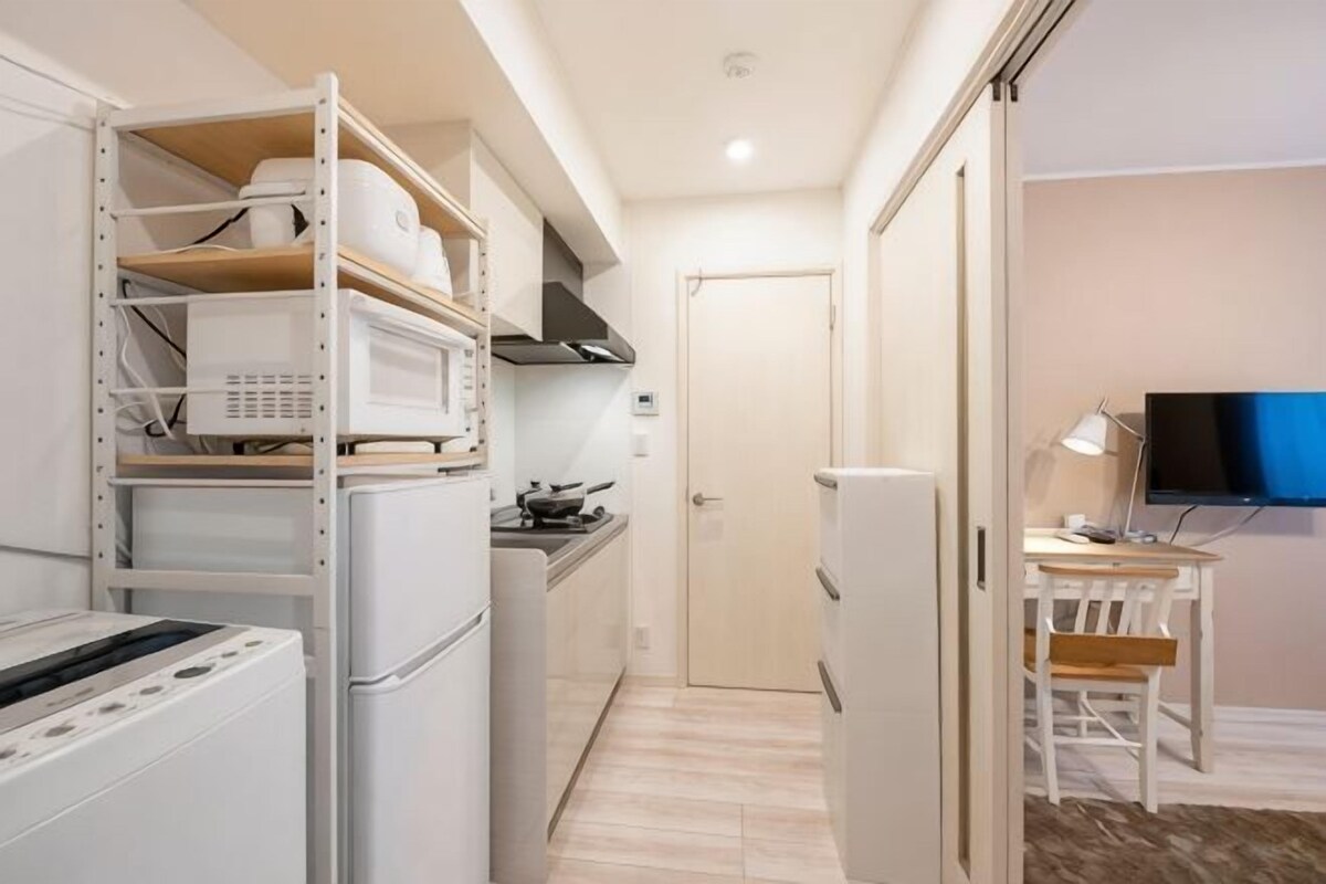 A compact kitchen with a microwave, stove, and refrigerator. There is a dining area with a table and chairs, and a television mounted on the wall.