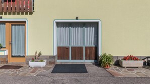 Una entrada de edificio con puerta de madera, un ventanal con cortinas y plantas en macetas.