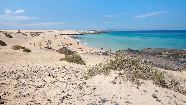 A beach with clear turquoise water, sandy areas, and rocky terrain.