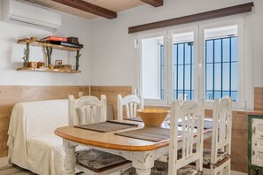Un coin repas avec une table en bois, des chaises blanches, un canapé blanc et une fenêtre avec des barreaux bleus.