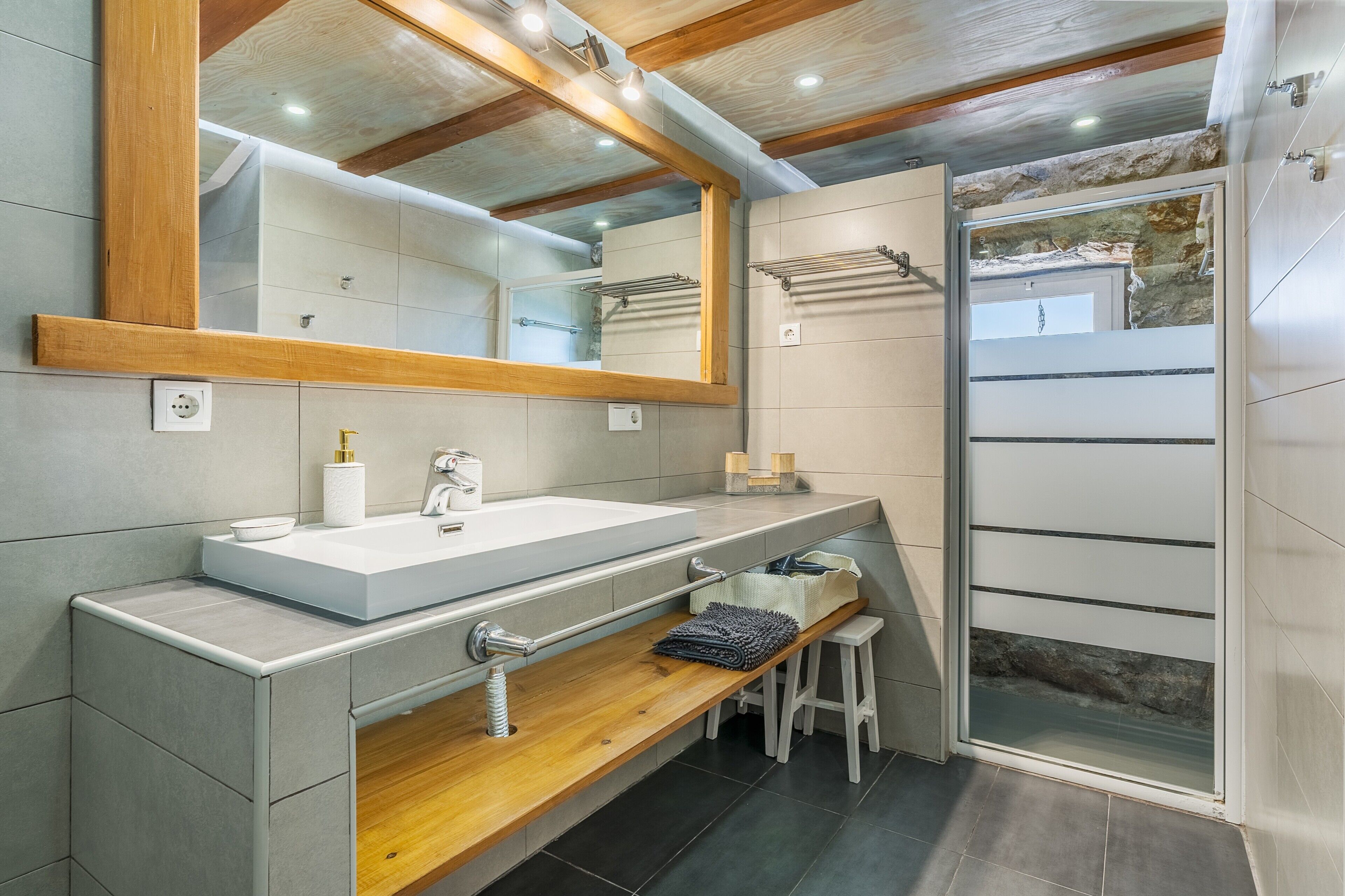 Une salle de bain moderne avec un grand miroir, un meuble-lavabo en bois, un espace douche et un banc.
