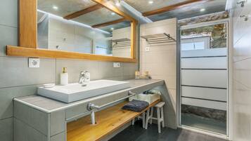 Une salle de bain moderne avec un grand miroir, un meuble-lavabo en bois, un espace douche et un banc.