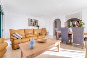 Ein modernes Wohnzimmer mit Ledersofa, Couchtisch aus Holz und Essbereich mit Stühlen und Tisch.