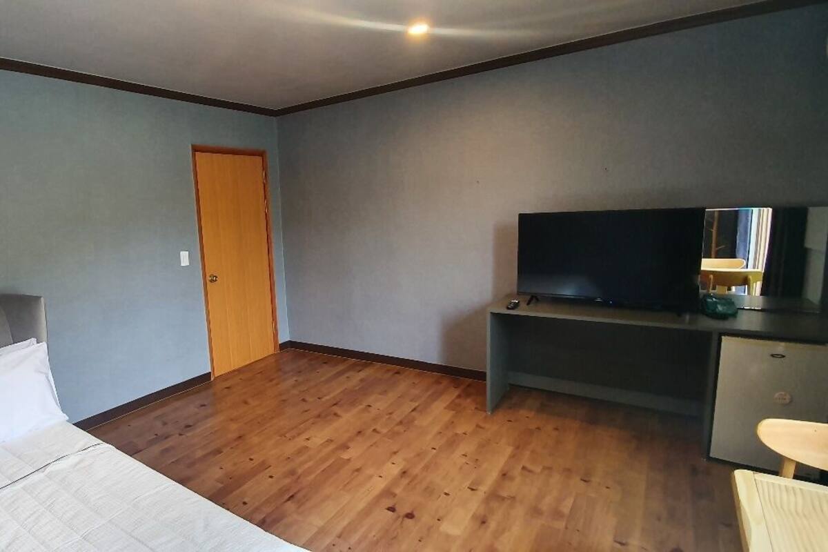 Una habitación de hotel con una cama, un televisor sobre un mueble, un escritorio y una puerta.