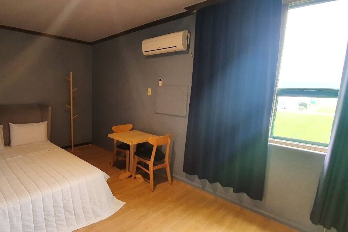 Un dormitorio con cama, escritorio, aire acondicionado y ventana con cortinas.