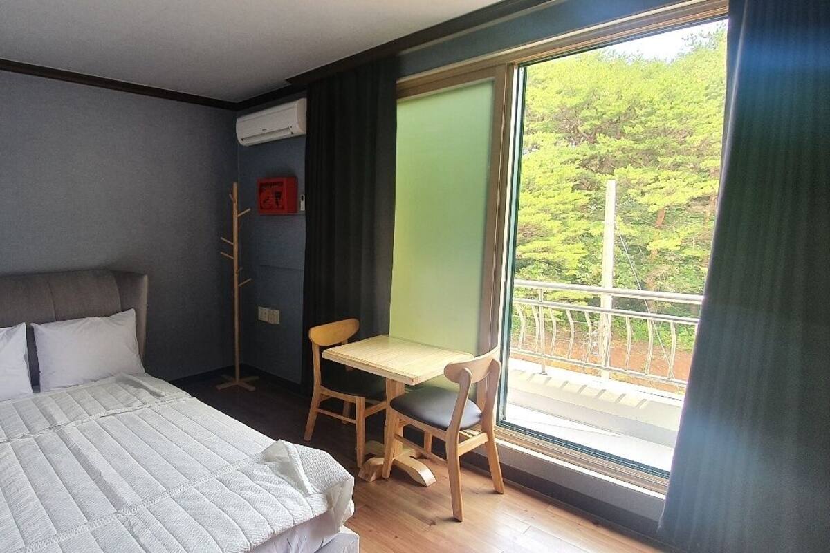 Un dormitorio con cama, escritorio y vista a zonas verdes por una ventana.