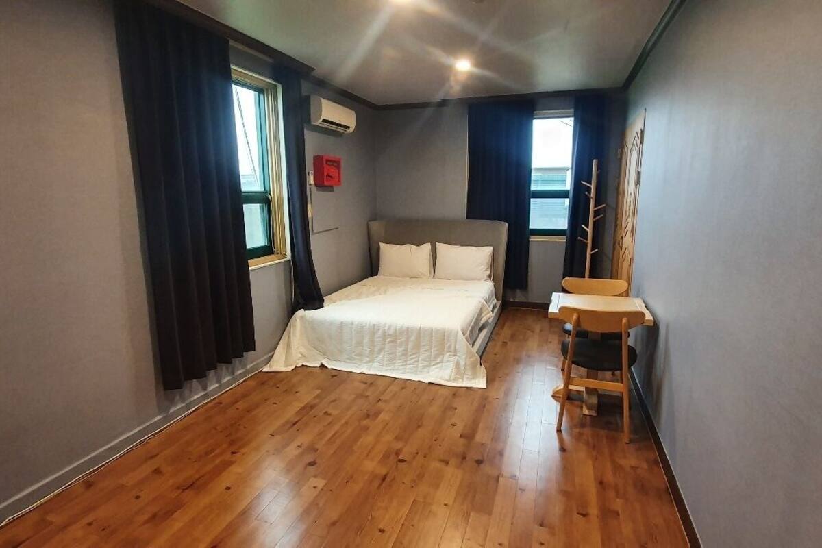 Un dormitorio con cama, una silla, un escritorio y ventana.