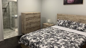 A bedroom with a bed, a wooden dresser, a nightstand, a shower, and a wall-mounted painting. - STONEHAVEN, perfect holiday accommodation for families. Close to GV Hospital (Shepparton)