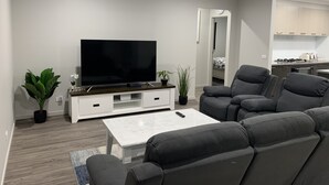 A modern living room with a flat-screen TV, grey sofas, a white coffee table, and a kitchen in the background. - STONEHAVEN, perfect holiday accommodation for families. Close to GV Hospital (Shepparton)