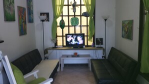 A living room with two green sofas, a TV on a stand, and artwork on the walls. - Manuela Antonio Comfort ocupado (Quepos)