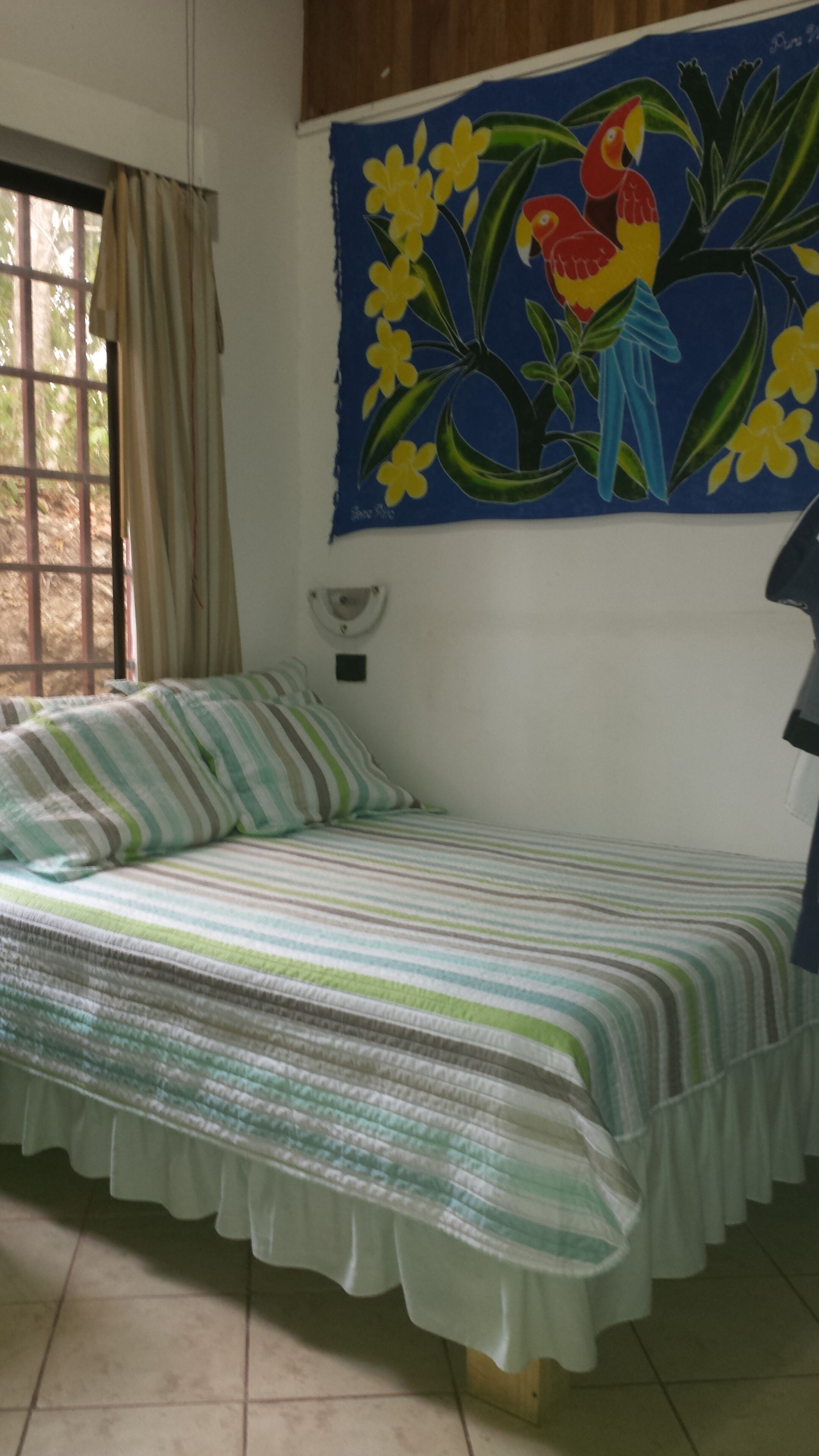 A room with a striped sofa, a window with a view of greenery, and a wall with a floral painting.