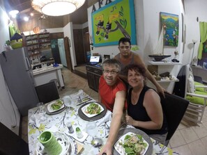 A dining area with a table set for three, a kitchen in the background, and artwork on the walls. - Manuela Antonio Comfort ocupado (Quepos)