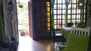 A room with a table, chairs, a window with a view of greenery, and a door with a decorative panel. - Manuela Antonio Comfort ocupado (Quepos)