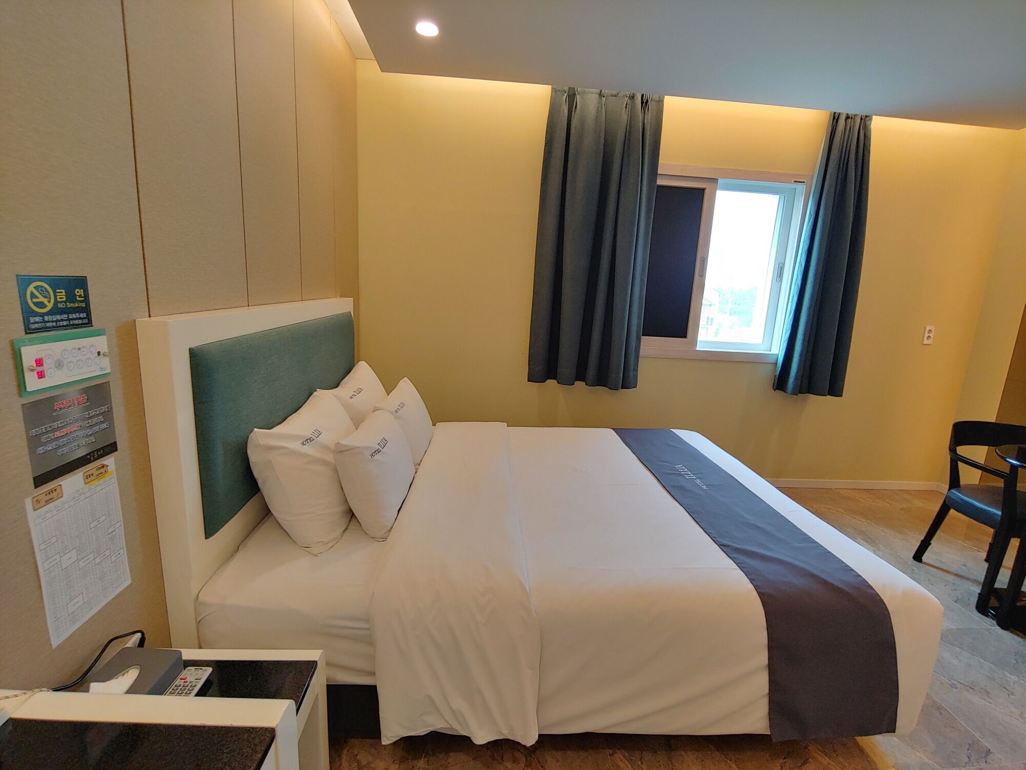 A hotel room with a bed, a desk with a telephone, and a window with curtains.