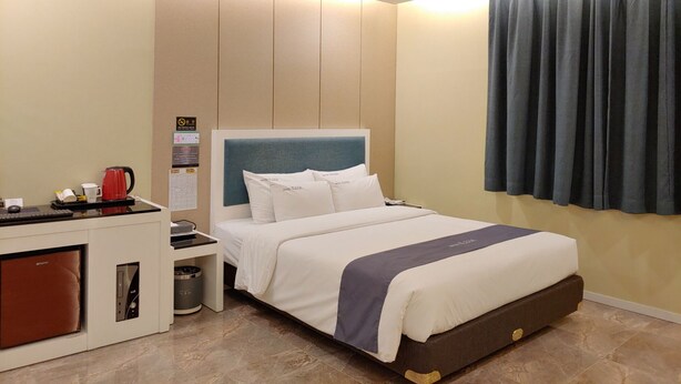 A hotel room with a bed, a desk with a coffee maker, a trash bin, and a control panel. - Jeju Ilua Hotel (Jeju City)