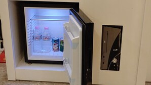A mini-fridge with a freezer compartment containing bottled water, a can of juice, and a carton of milk. - Jeju Ilua Hotel (Jeju City)