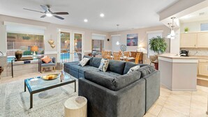 A spacious living room with a grey sectional sofa, a glass coffee table, and a dining area with wooden chairs. - Pool & Golf Cart: Sun City Grand Home! (Surprise)