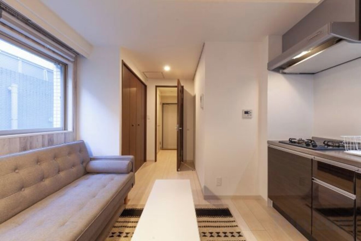 A compact living space with a sofa, a dining table, a kitchen area with a stove, and a window providing natural light.