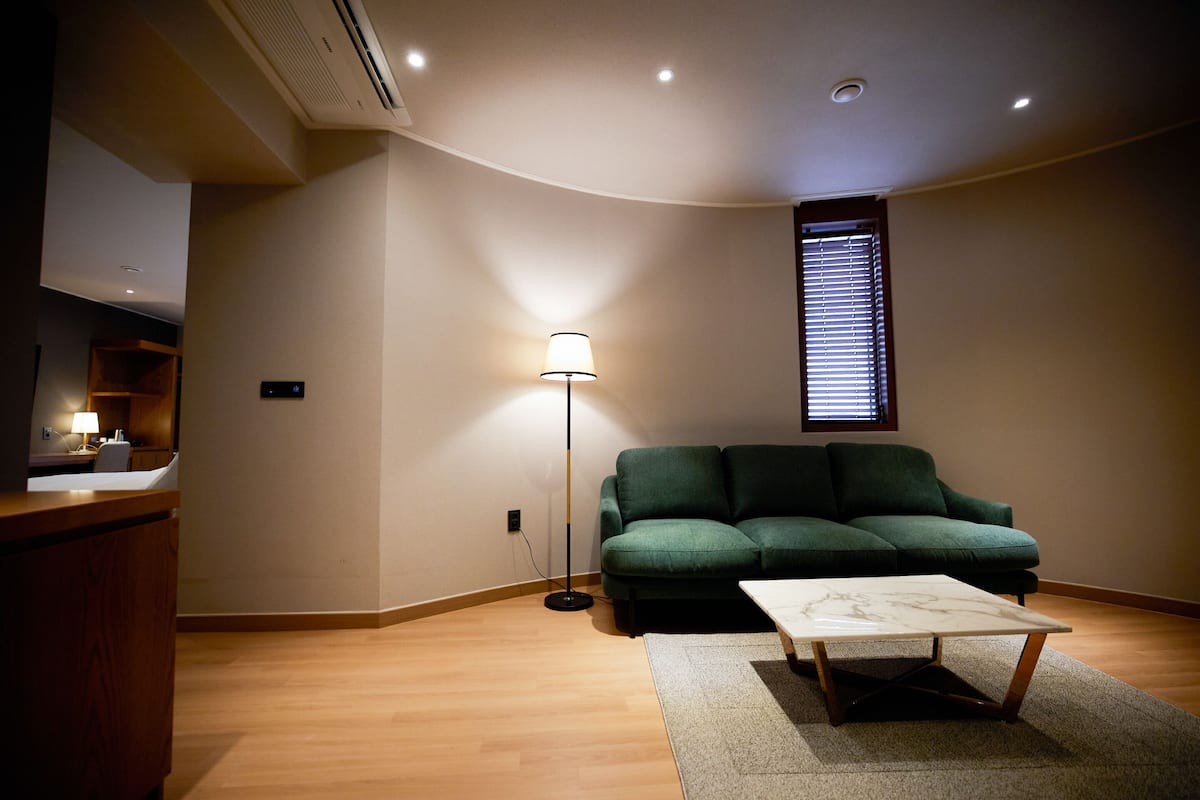A living room with a green sofa, a coffee table, a floor lamp, and a window with blinds.