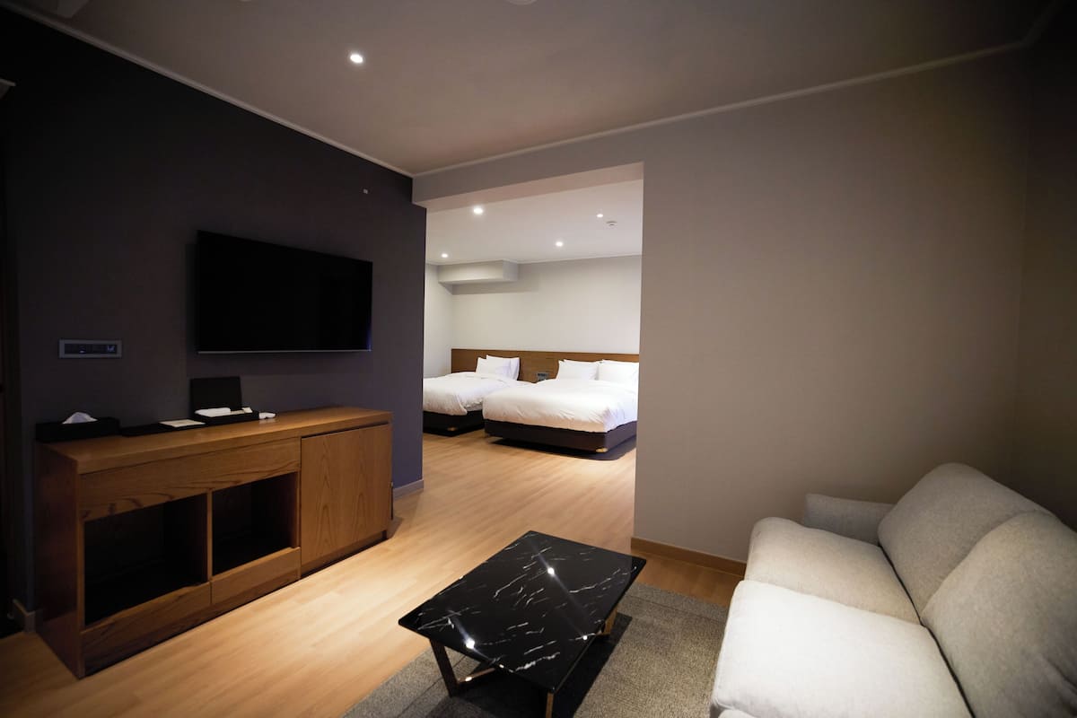 A modern hotel room with a flat-screen TV, wooden console, a black marble coffee table, a sofa, and a bed with white bedding.