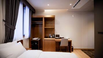 A hotel room with a bed, a desk with a chair, a wardrobe, and a bedside table.