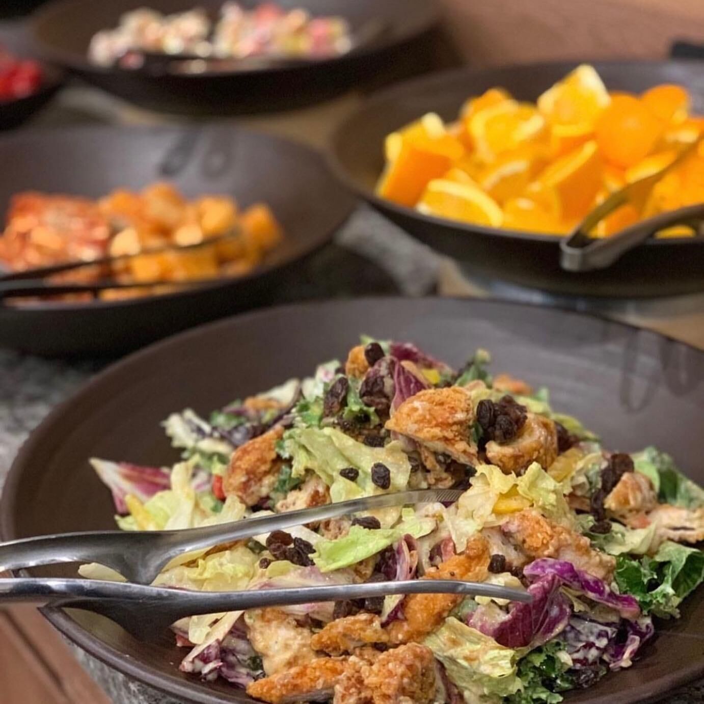 A salad with croutons and nuts, a bowl of sliced oranges, and a pan with food.