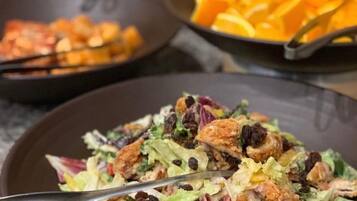 A salad with croutons and nuts, a bowl of sliced oranges, and a pan with food.