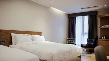 Quarto de hotel com duas camas, cabeceira de madeira, escrivaninha com cadeira e uma janela grande com cortinas.