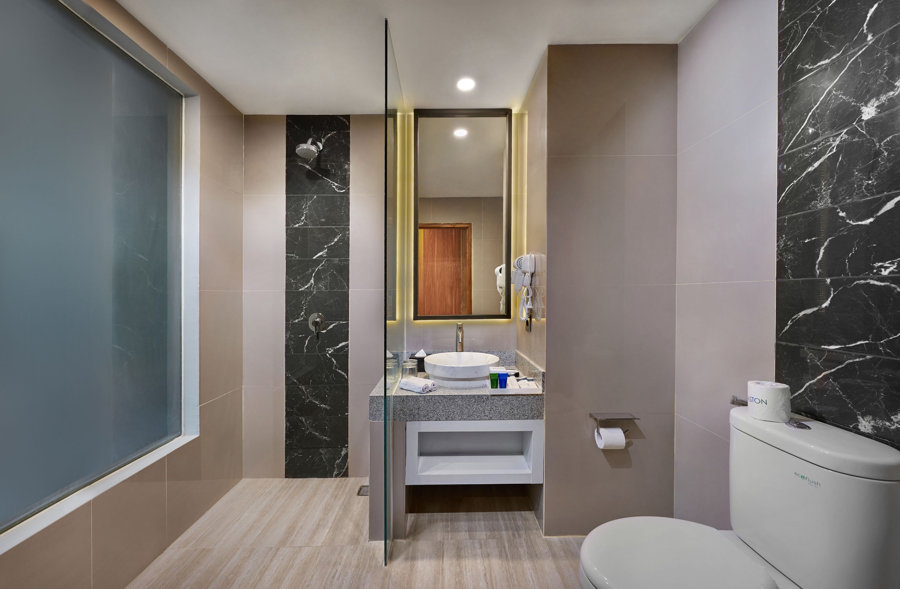 A modern bathroom with a glass partition, a marble-tiled wall, a white sink, and a toilet.